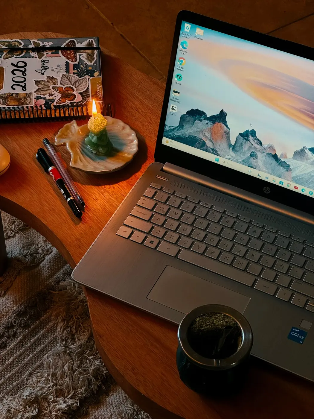 Mesa de trabajo con una laptop, un mate y una vela encendida